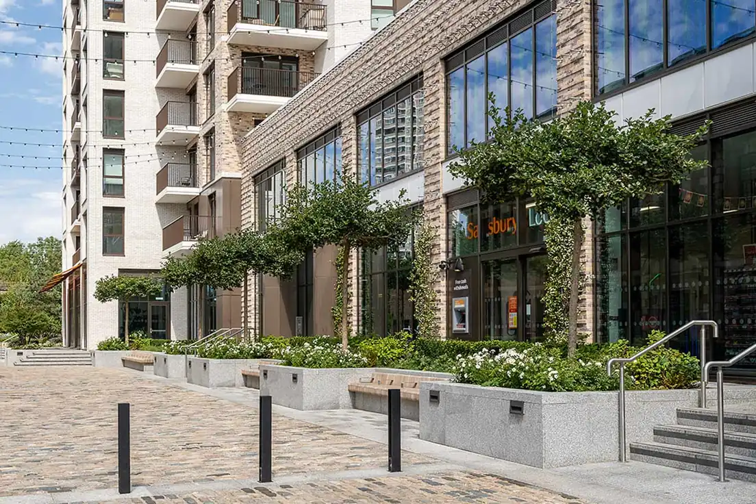 Apartment buildings at Bow Green with shops, planted beds and benches along a cobbled street