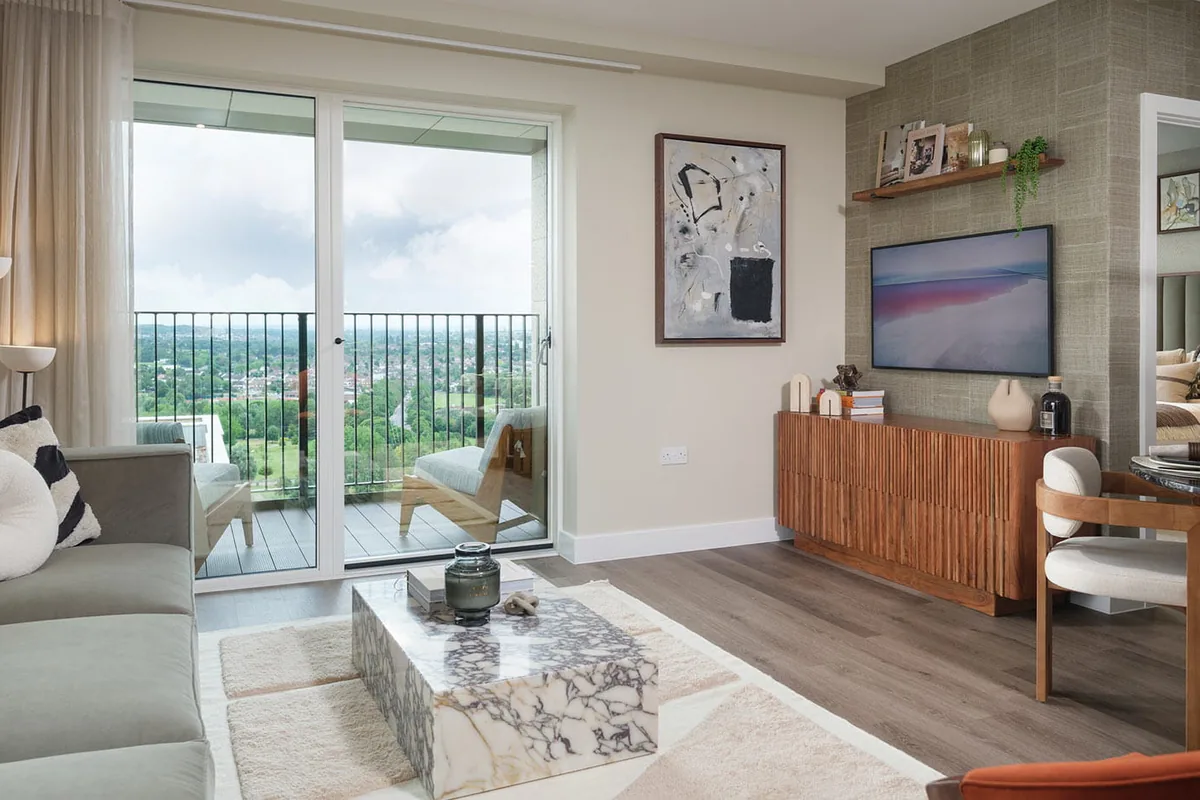 Kidbrooke Village’daki Central Gardens’ta kanepe, mermer sehpa ve ağaçlara bakan balkona açılan cam kapıları olan bir salon.