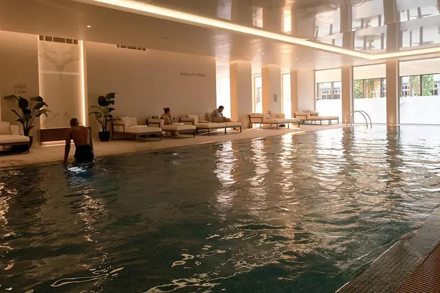 Royal Arsenal Riverside’daki The Waterside Club’da içinde bir yüzücü bulunan, kenarında şezlonglar olan kapalı yüzme havuzu.