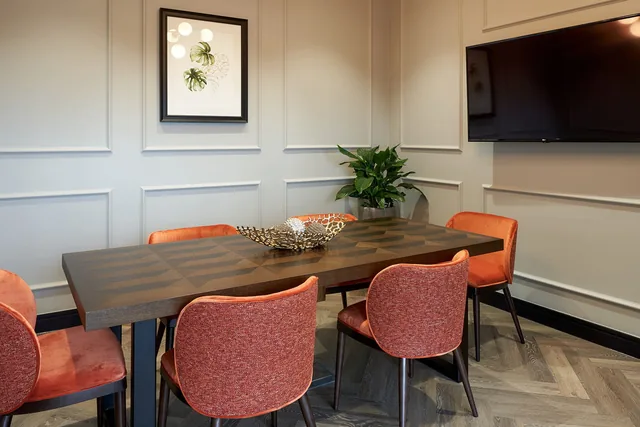 A meeting room at The Parkside Club, The Green Quarter, with a wooden table, orange chairs and a wall-mounted screen.