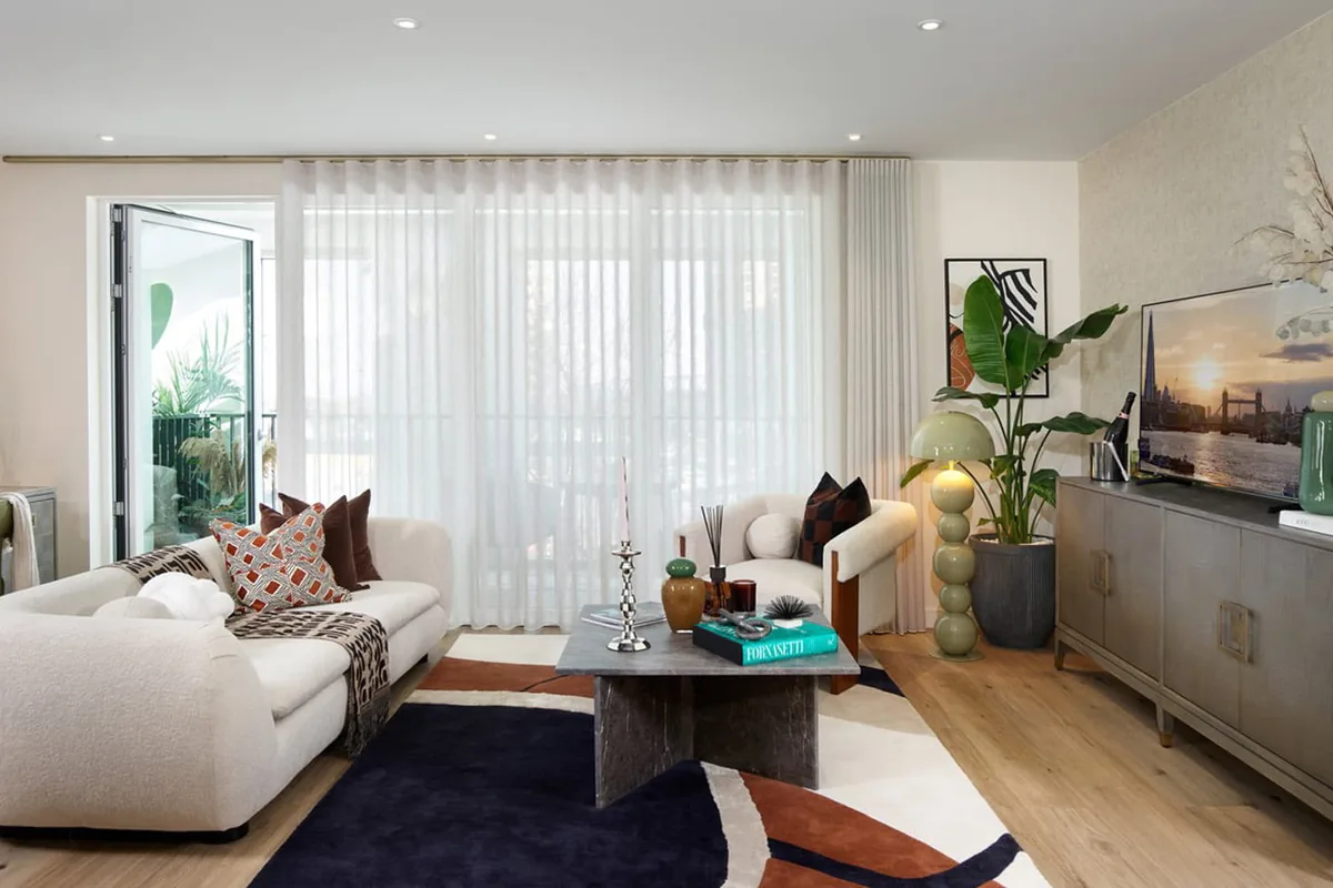The living room of the two-bedroom show apartment at The Green Quarter, with a cream sofa, a coffee table and sheer curtains over full-height windows.