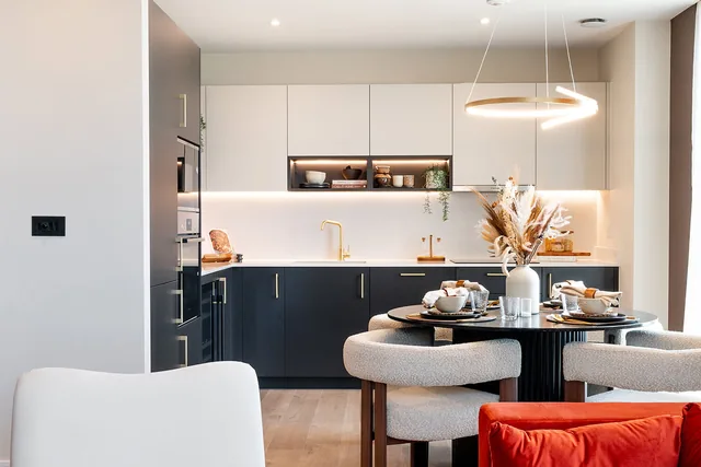 A kitchen with dark lower units and a round dining table in the three-bedroom show apartment at TwelveTrees Park.