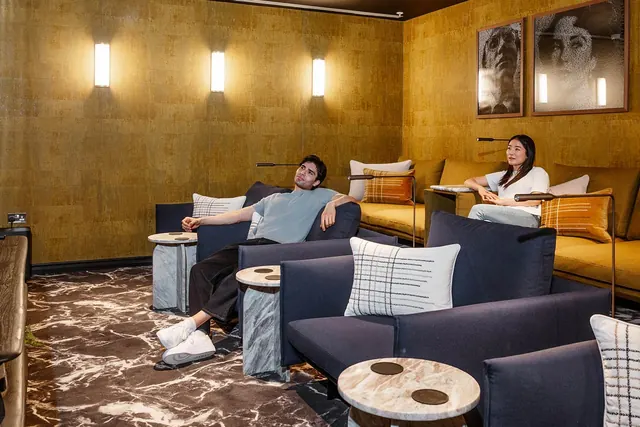 Two people relaxing on sofas and armchairs in the cinema room at TwelveTrees Park.