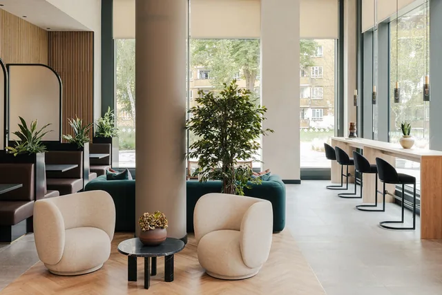 A communal study space at Woodberry Down with armchairs, a high counter with stools and floor-to-ceiling windows.