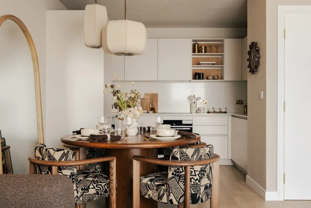 A round dining table with patterned chairs in front of the kitchen in the one-bedroom show apartment at Woodberry Down.