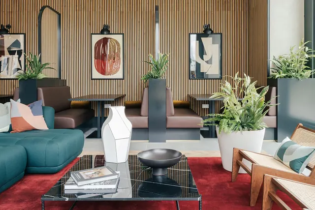 The residents’ lounge at Woodberry Down with sofas, booth seating, plants and a red rug.