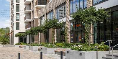 Apartment buildings at Bow Green with shops, planted beds and benches along a cobbled street